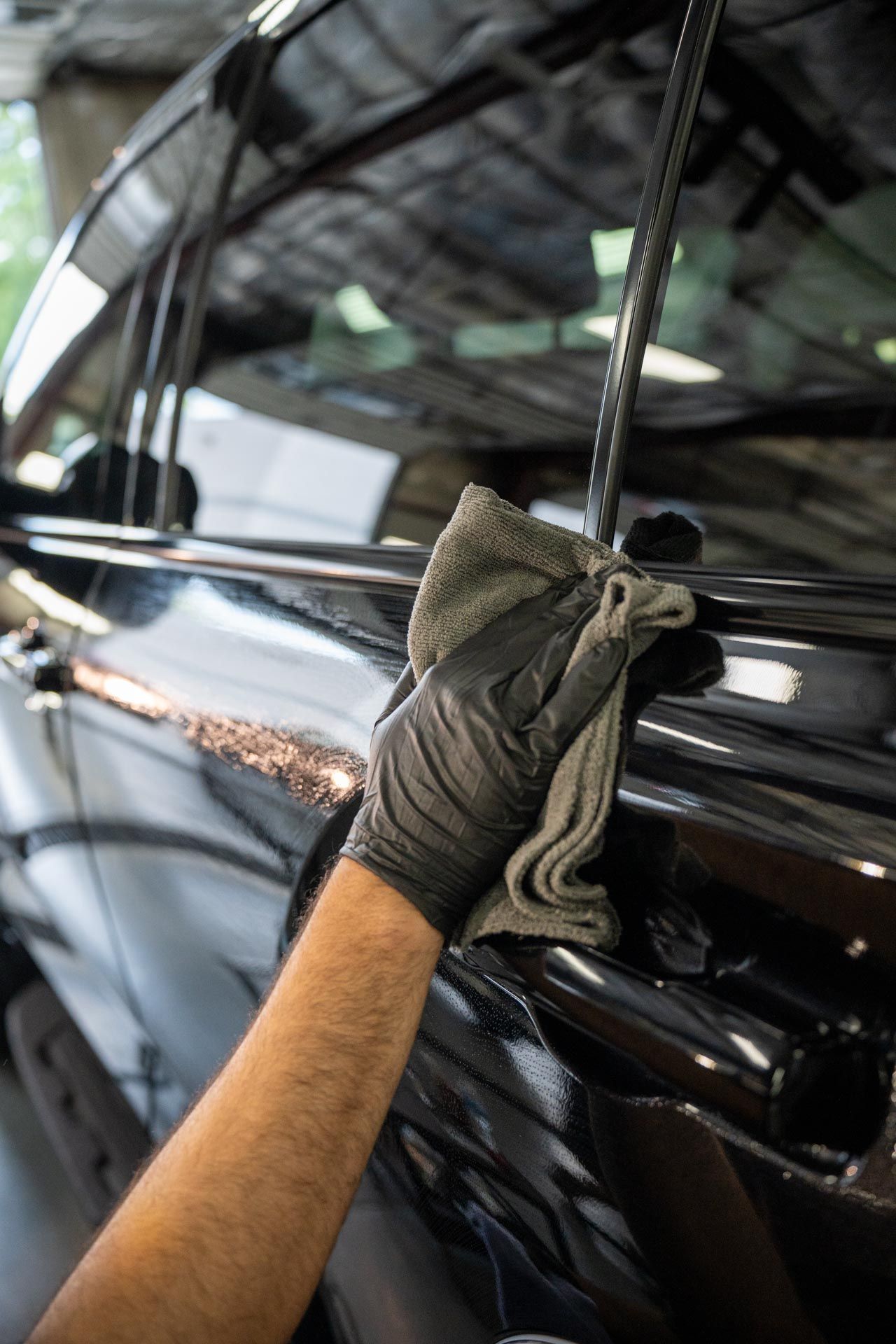 A person is cleaning a car with a towel and gloves.