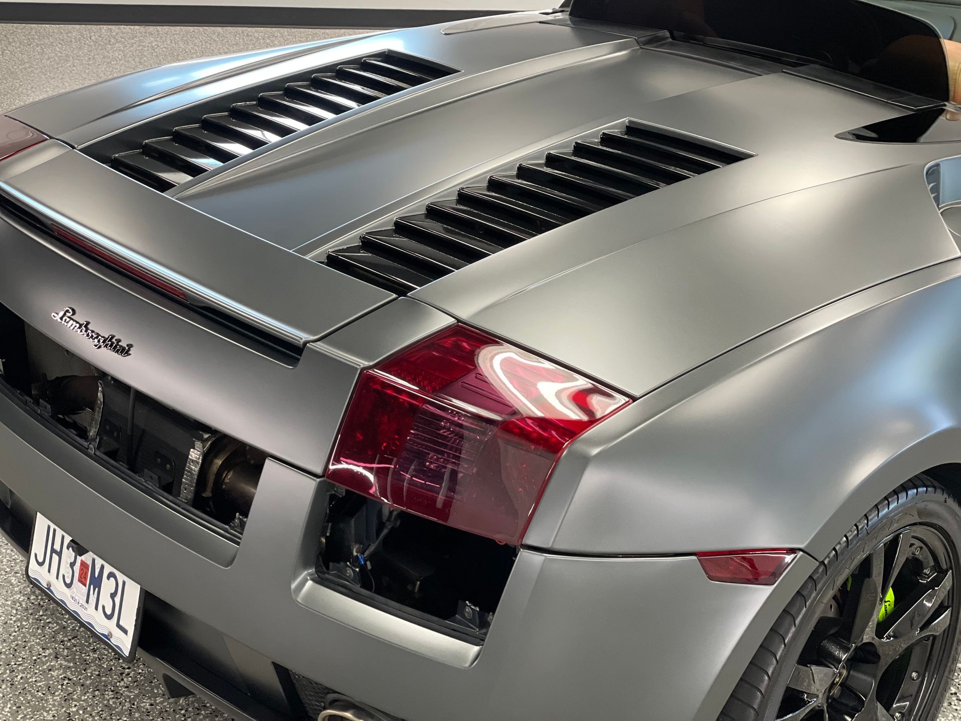 The rear end of a gray lamborghini is shown.