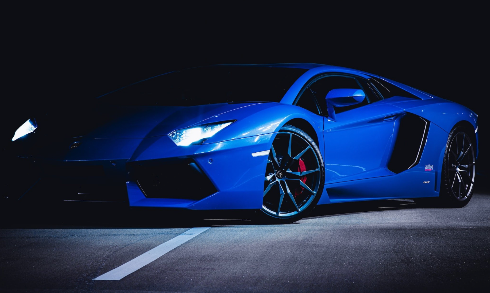 A blue lamborghini aventador is parked in a parking lot at night.