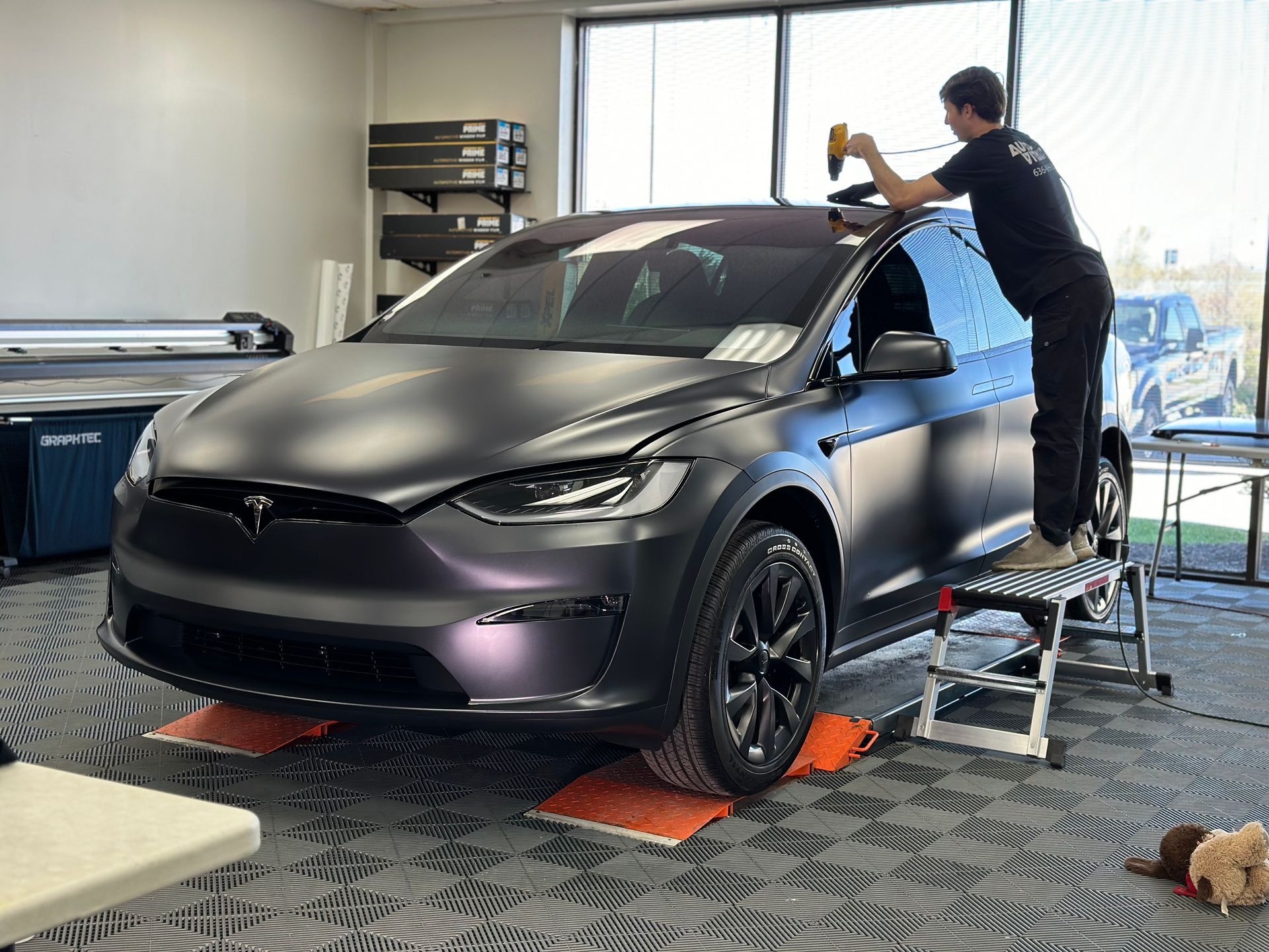 A man is wrapping a tesla model x in a matte black wrap.