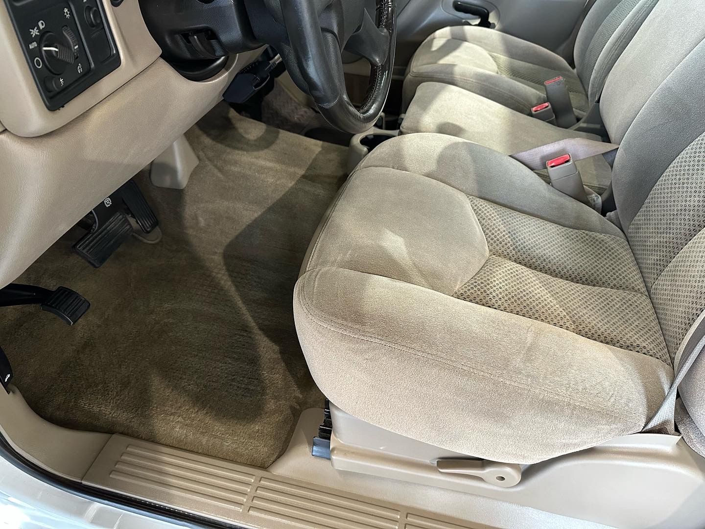 A close up of a car seat with a steering wheel in the background.