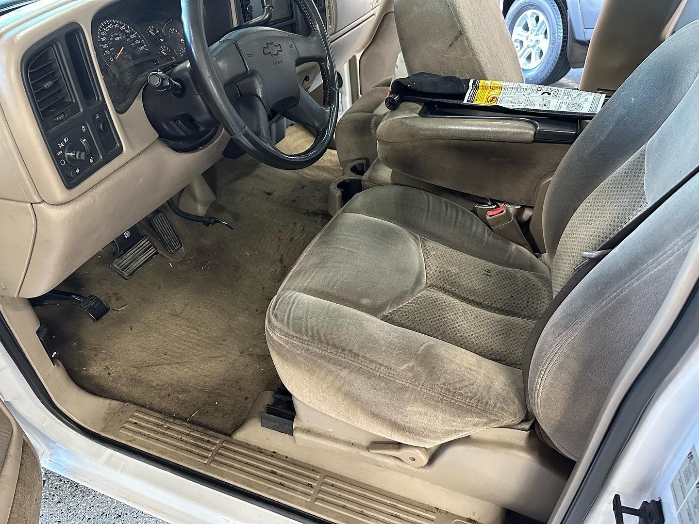 The inside of a white car with a dirty seat and a dirty steering wheel.