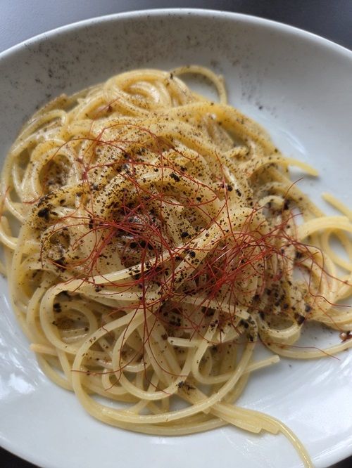 Spaghetti in una ciotola bianca, conditi con fiocchi di peperoncino rosso e spezie nere.