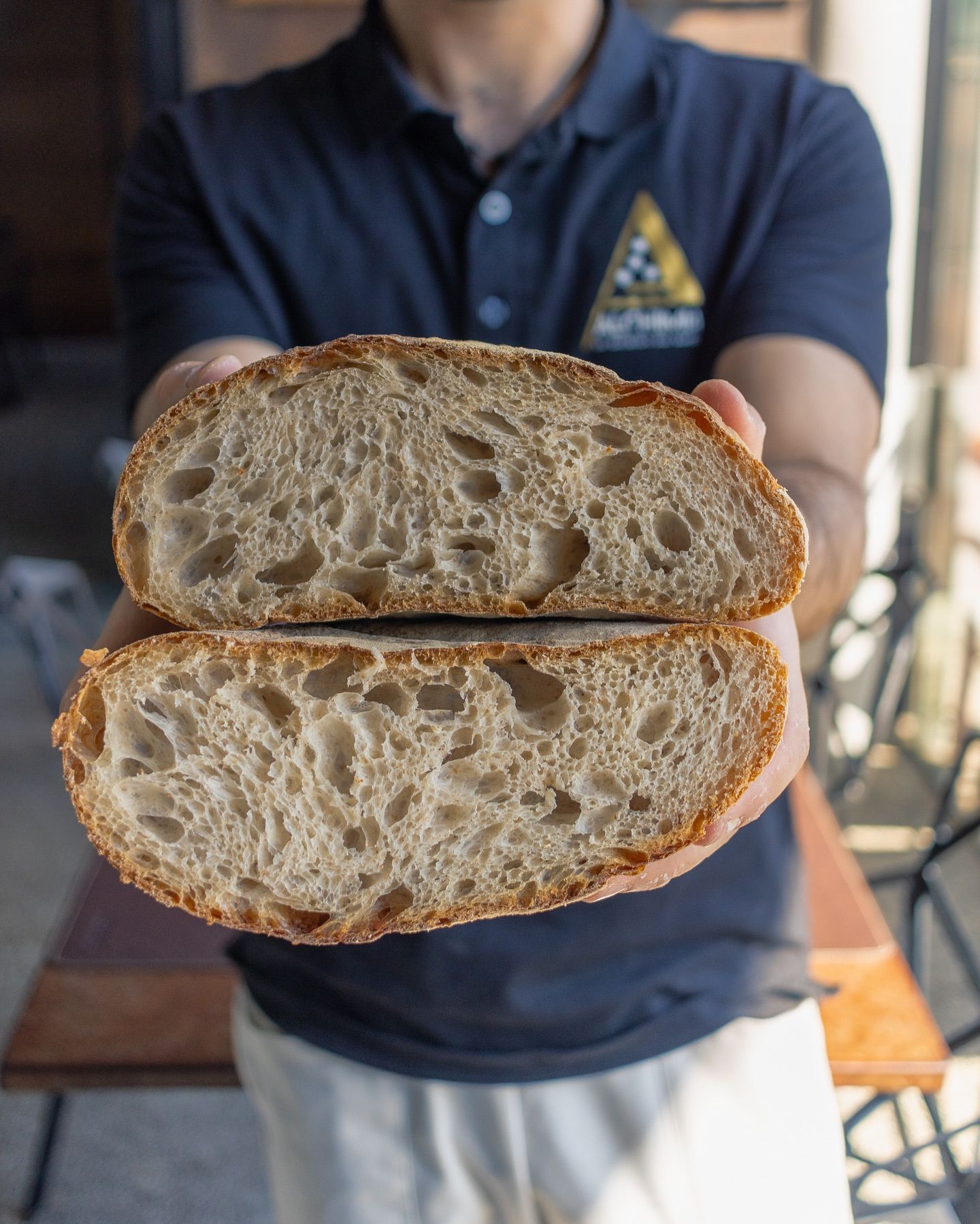 Uomo che tiene in mano due metà di una pagnotta rustica, mostrando l'interno arioso e l'esterno croccante.