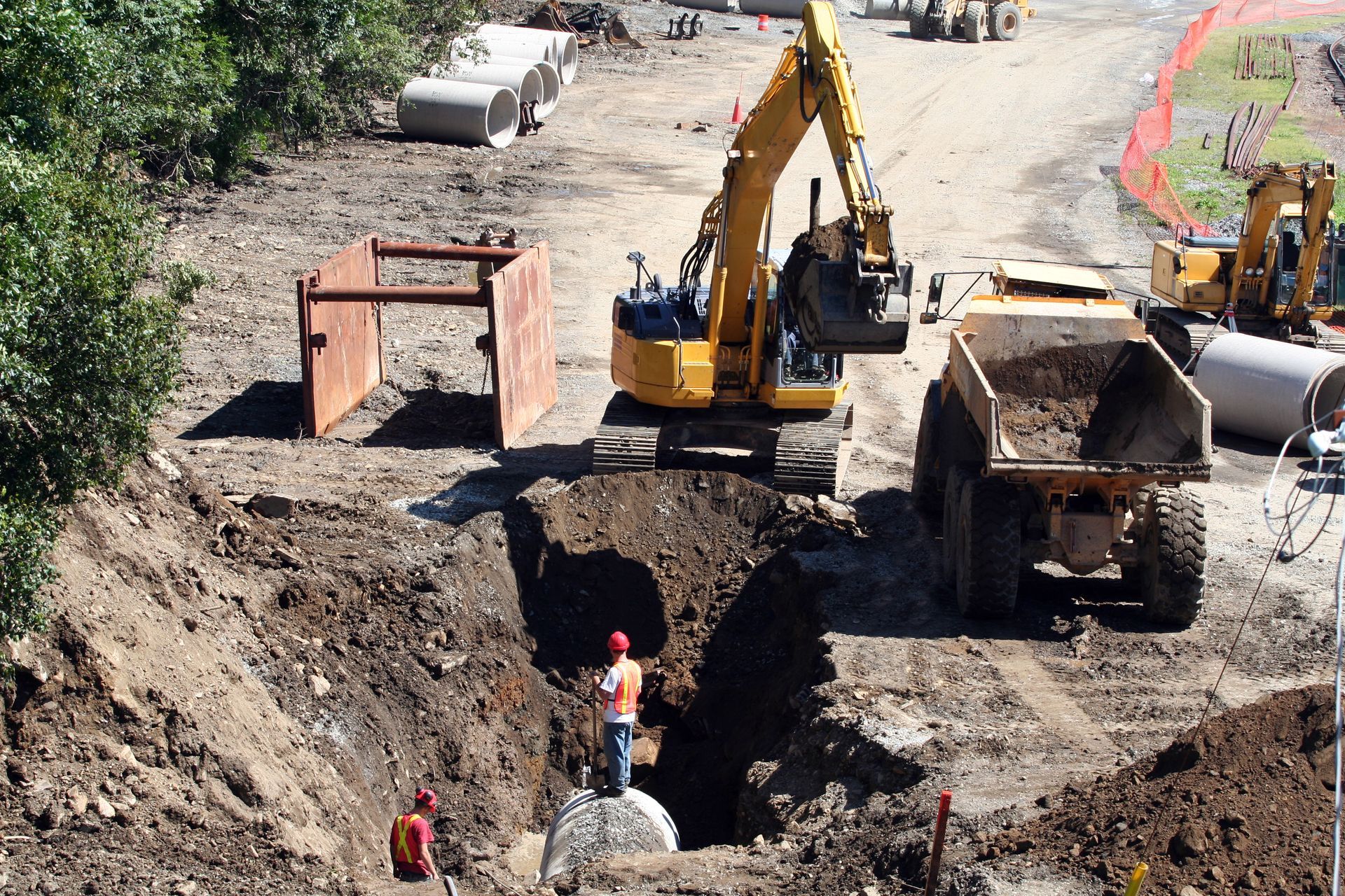Construction site with excavator and dump truck. Workers in hole.