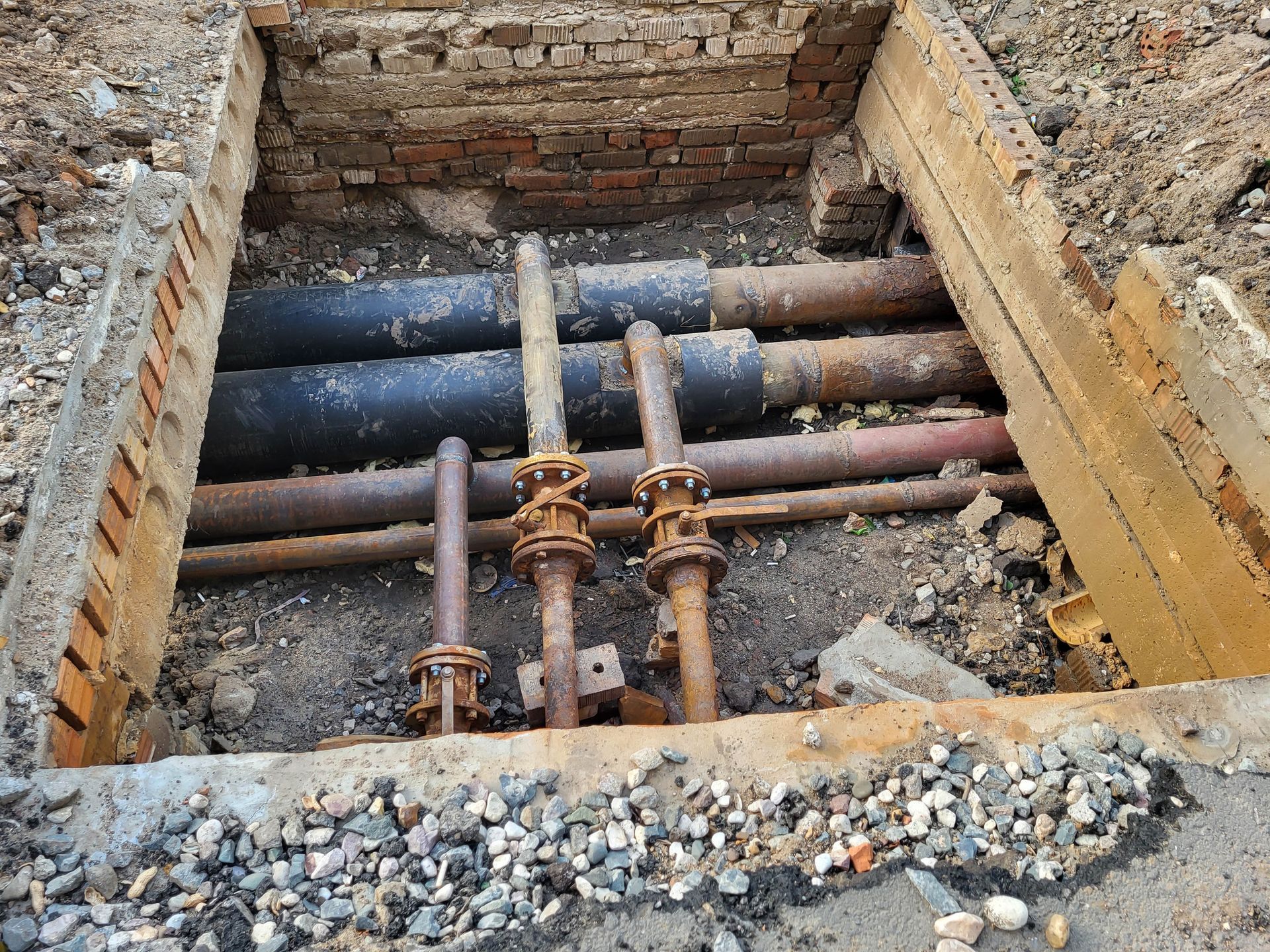 Pipes in a rectangular trench with brick and concrete surrounding, showing construction or repair work.