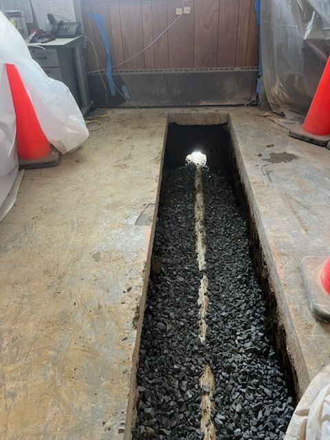 Concrete floor with a narrow trench filled with gravel. Two traffic cones are present.