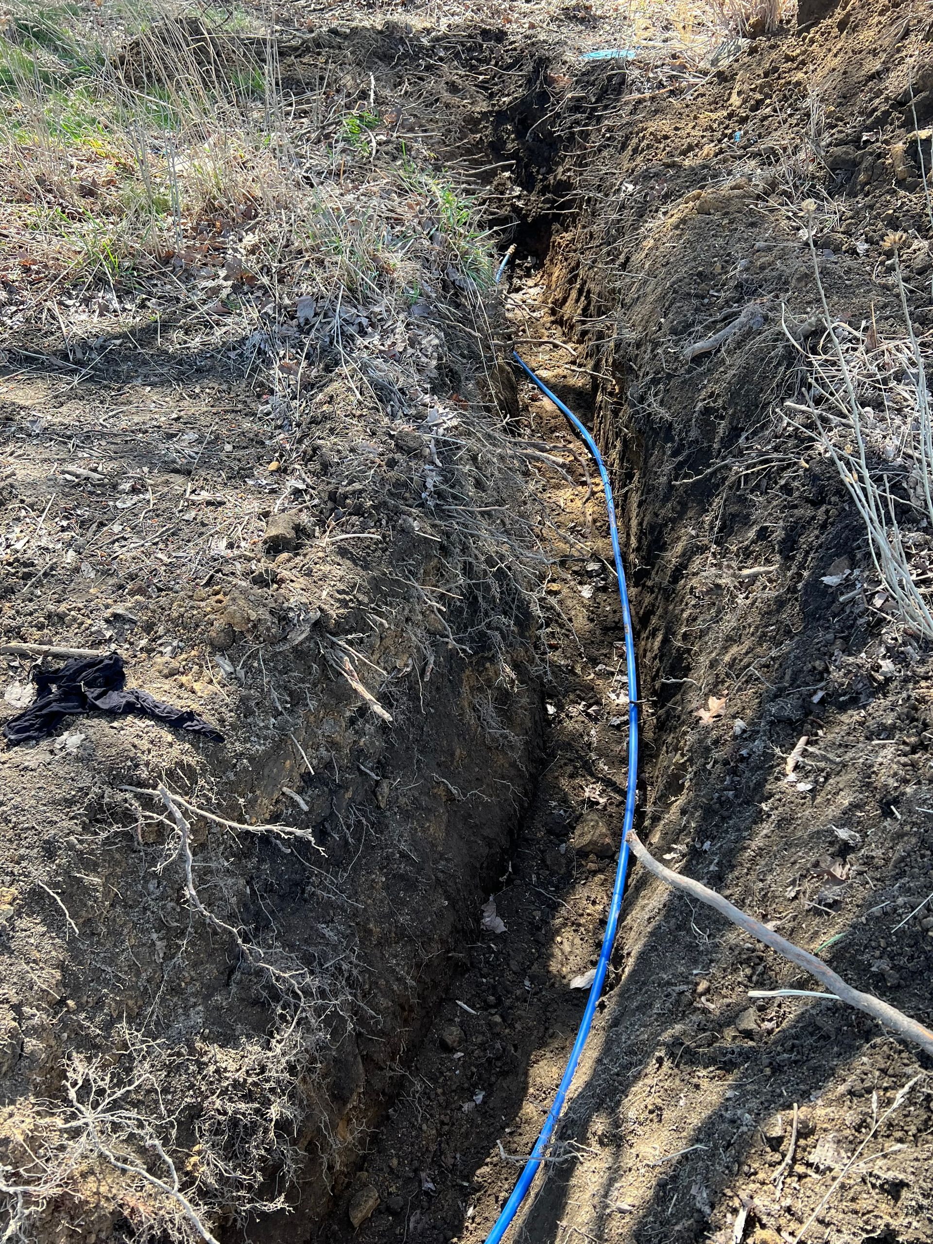 A narrow trench with a blue cable running through it, likely for utilities, in an outdoor setting.