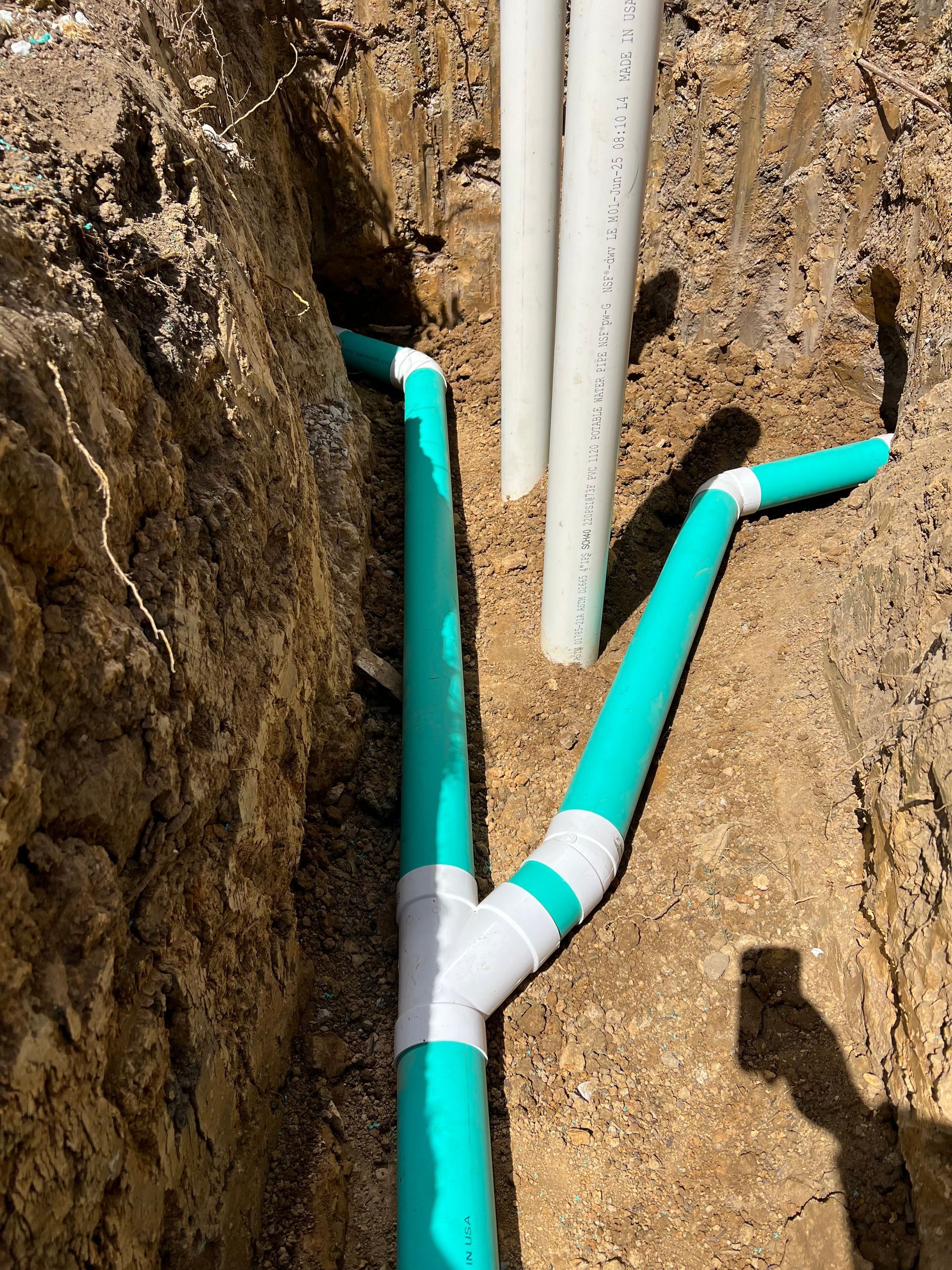 Green and white pipes in a trench. Plumbing pipes are installed underground.