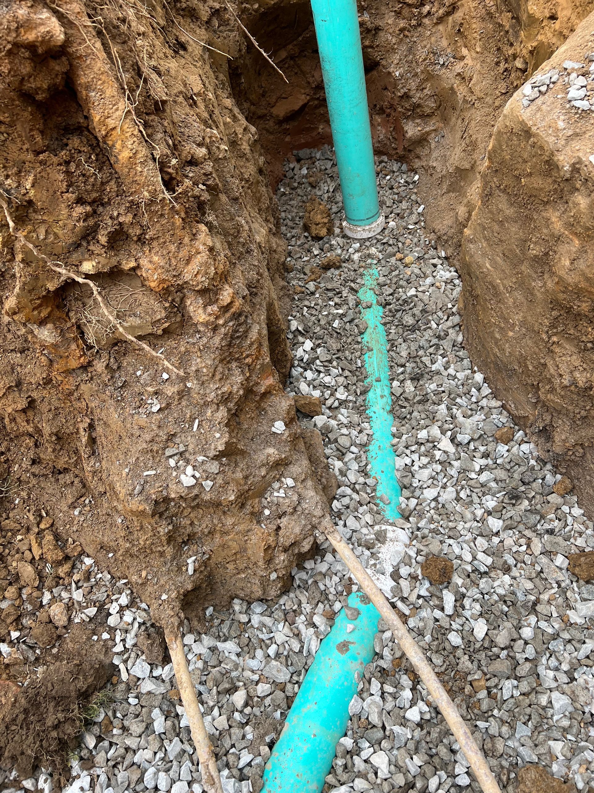 Green pipes in a gravel-lined trench, surrounded by soil.