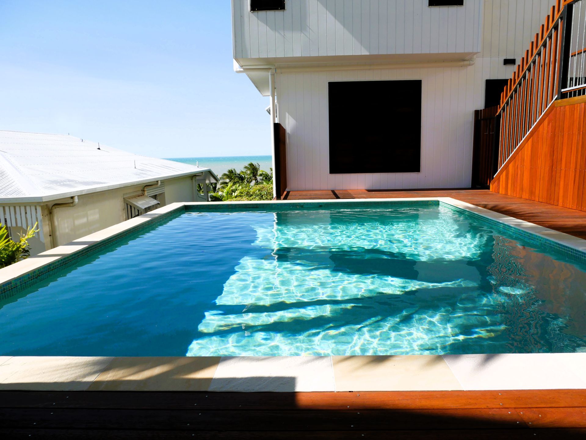 A Swimming Pool with A Wooden Deck and Chairs Around It — Pools Plus NQ in Cairns, QLD