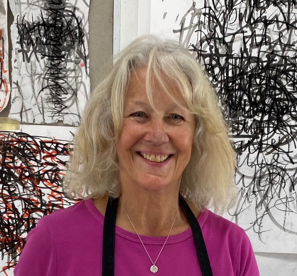 A man with a beard is standing in front of two paintings