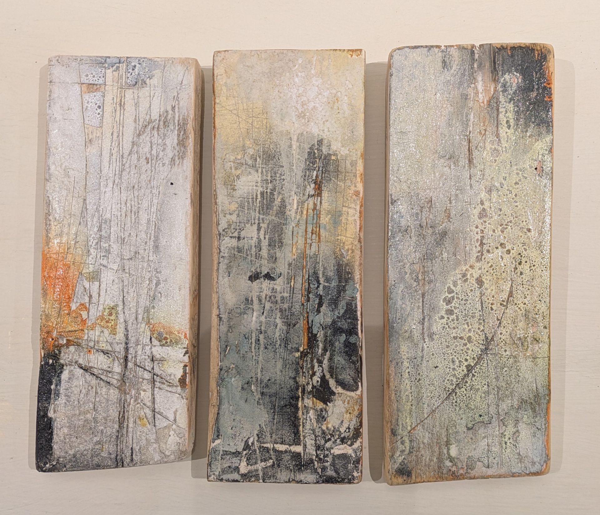 Three abstract painted wooden panels in muted beige, gray, and orange tones