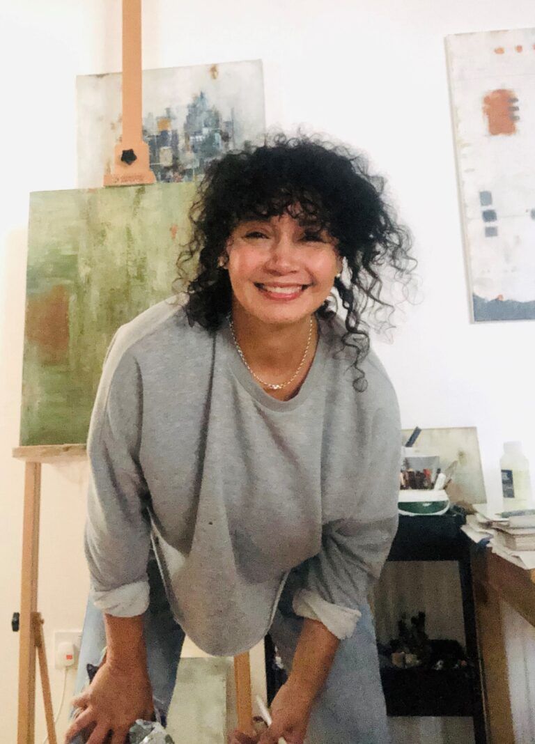 A woman with curly hair is smiling in front of an easel
