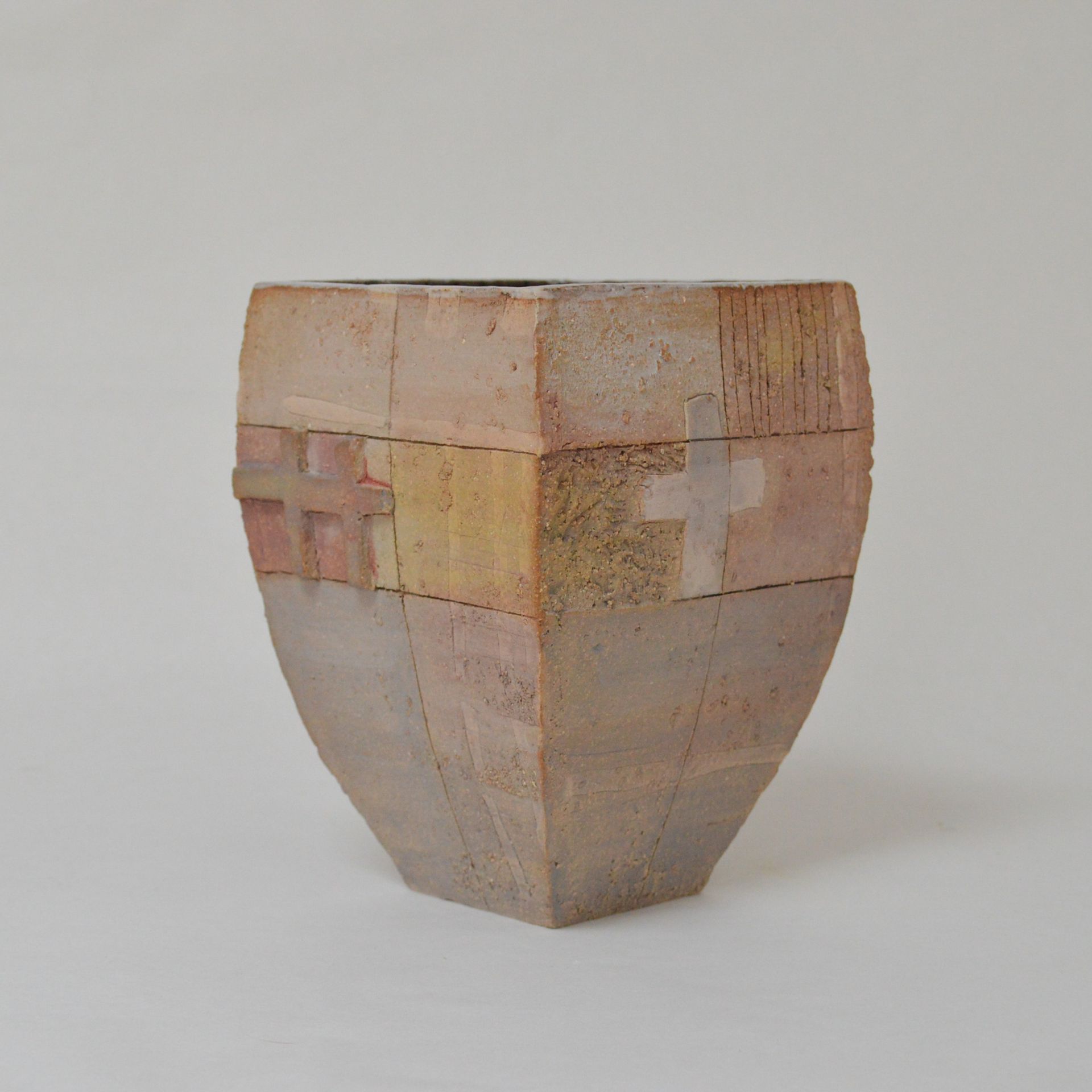 A square, tapered ceramic vase with a textured, multi-toned tan surface featuring carved cross symbols on two sides.