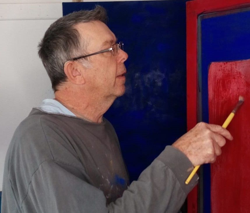 A man wearing glasses is painting a red and blue picture