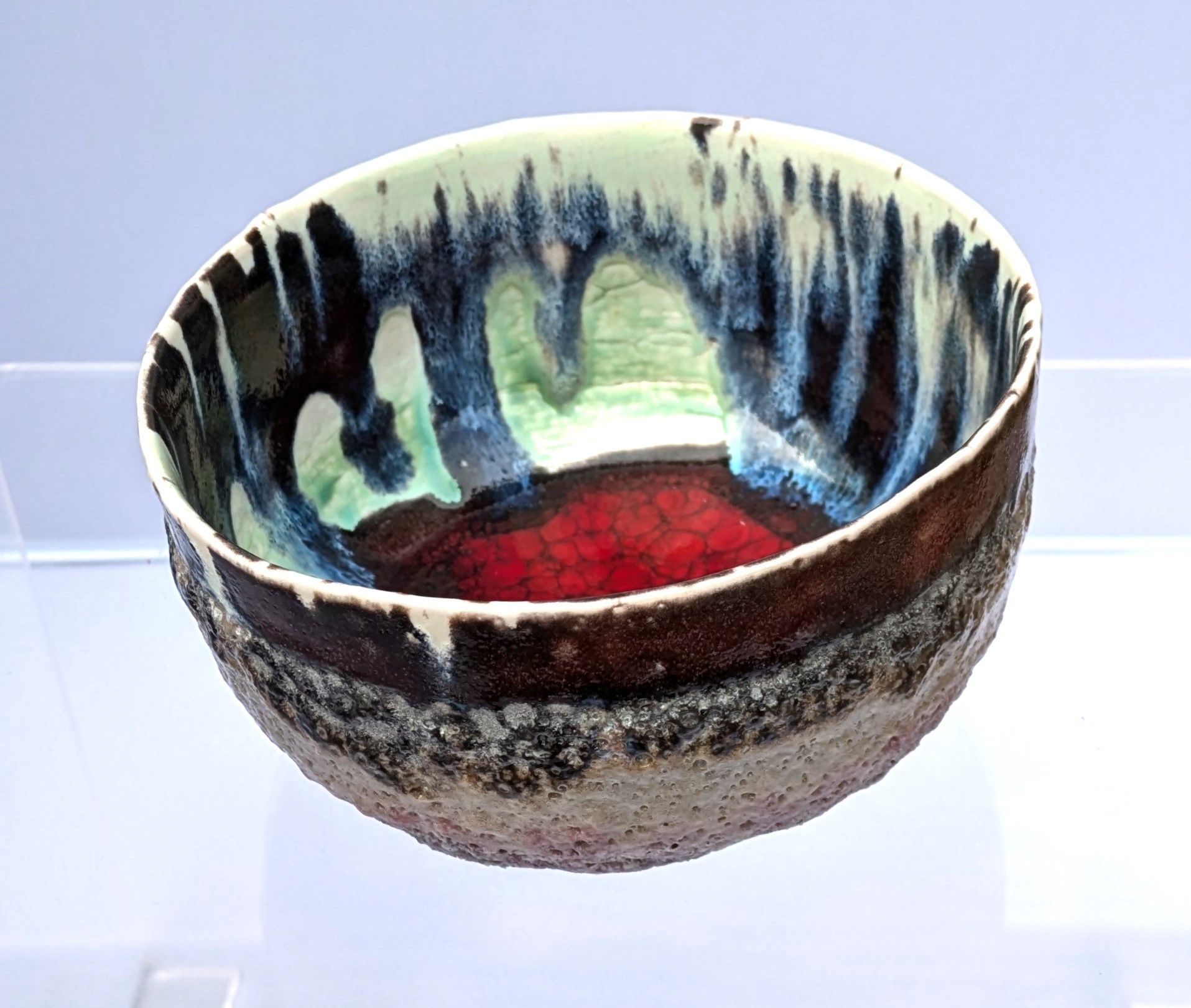 Ceramic bowl with textured, multi-colored glaze: dark blue, green, red, and brown.