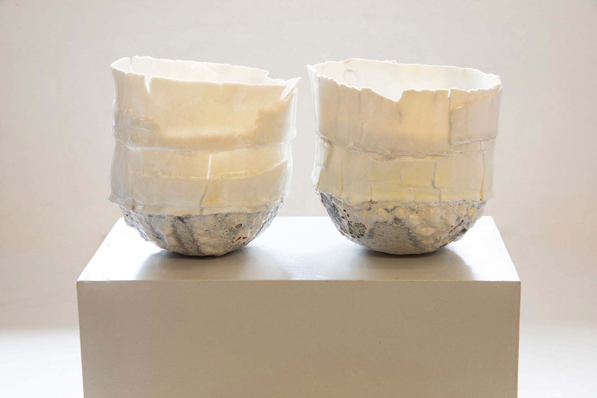 Two white bowls are sitting on top of a white cube.