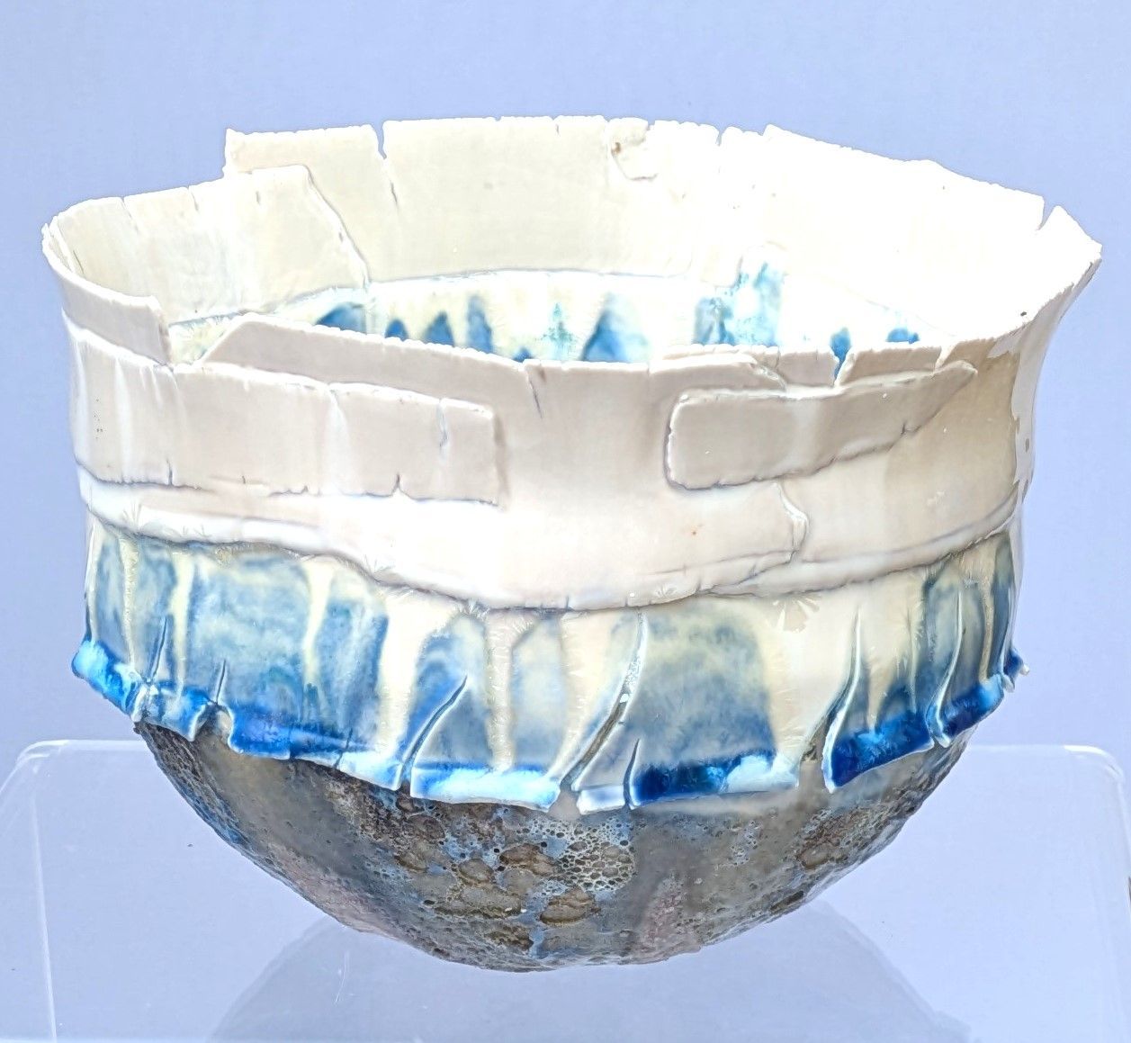 A white and blue bowl is sitting on a glass shelf