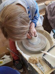 A woman is making a cup on a pottery wheel.