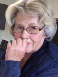 A woman wearing glasses and a blue sweater is biting her nails.