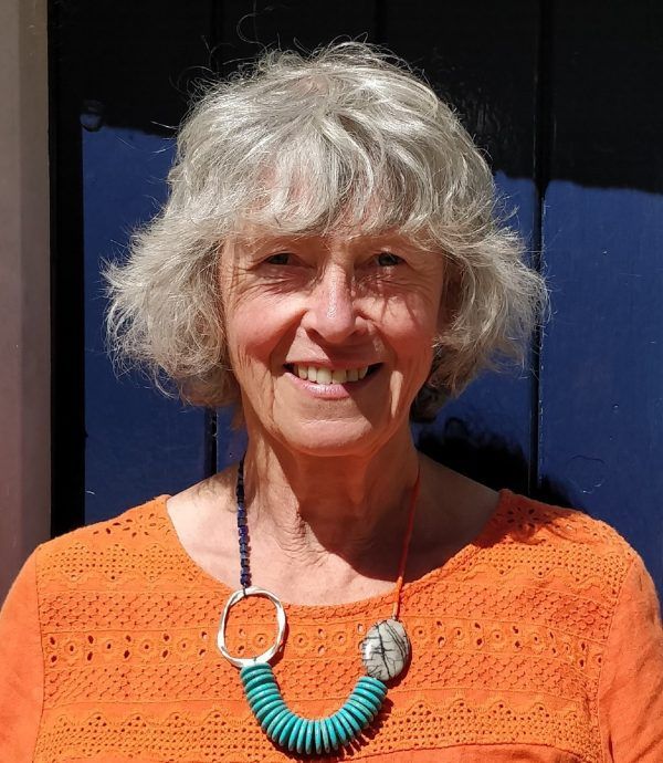 A woman wearing an orange shirt and a turquoise necklace is smiling.
