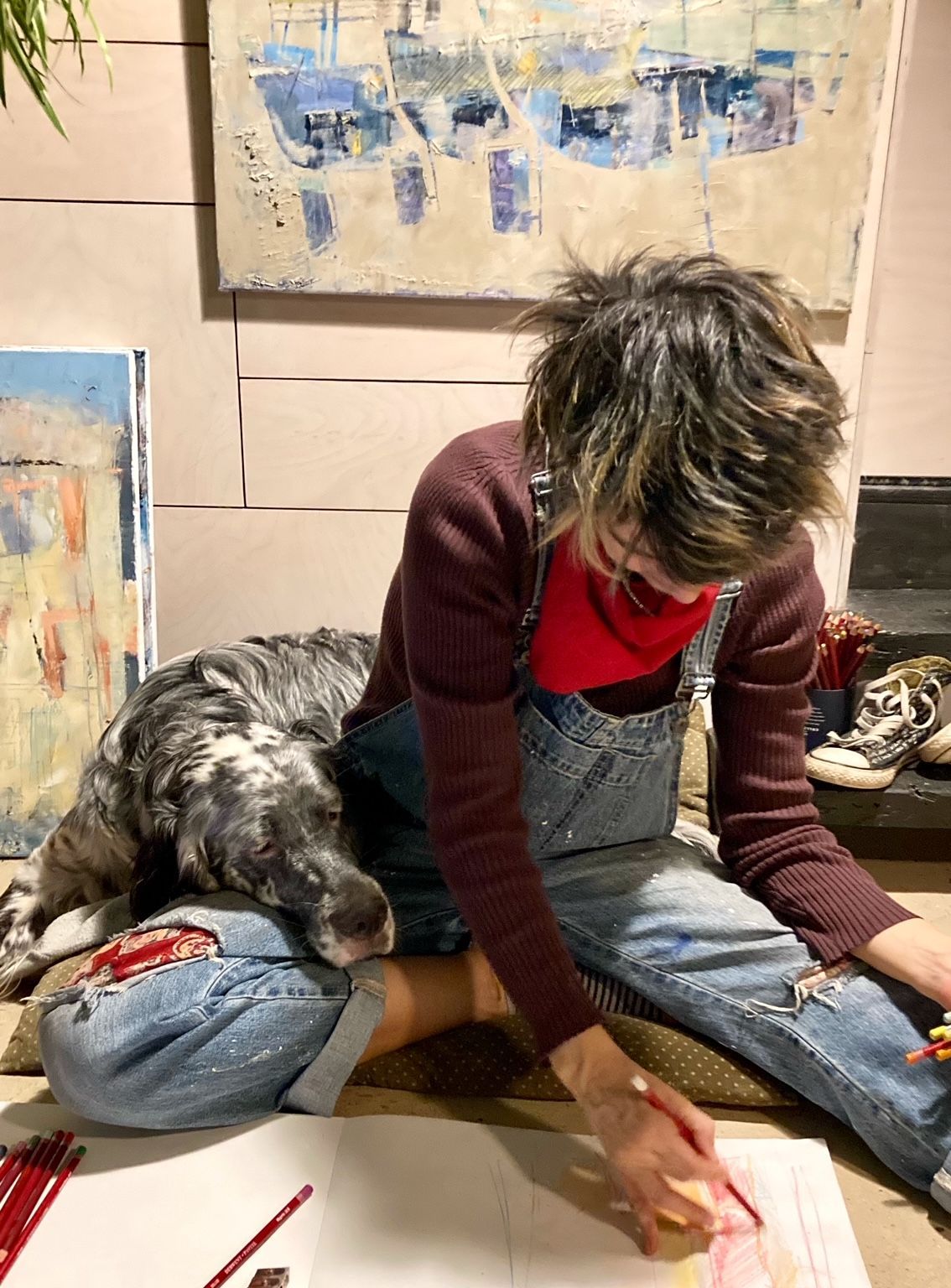 A woman is sitting on the floor painting with a dog.