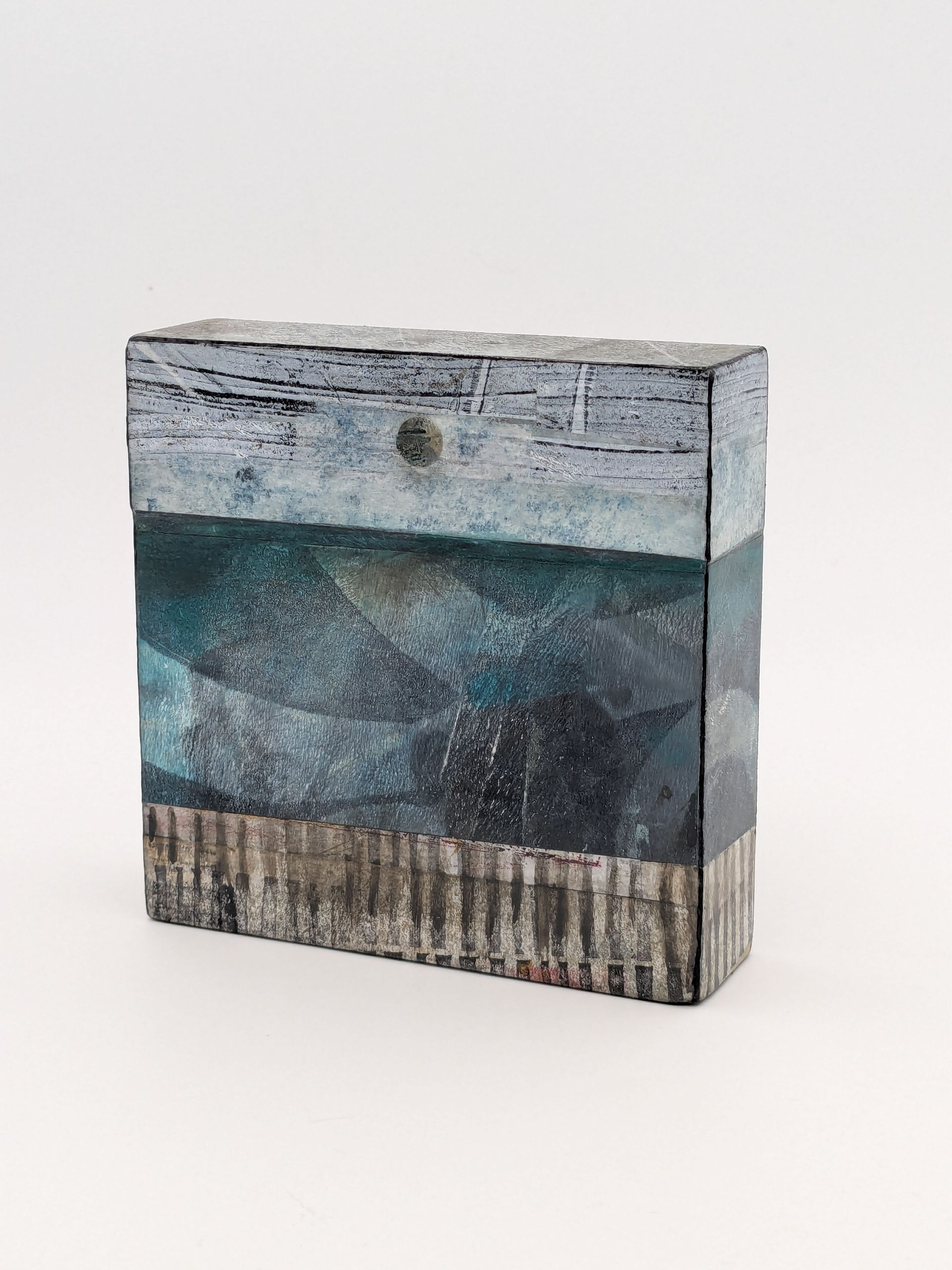 A square block with a painting on it is sitting on a white surface.