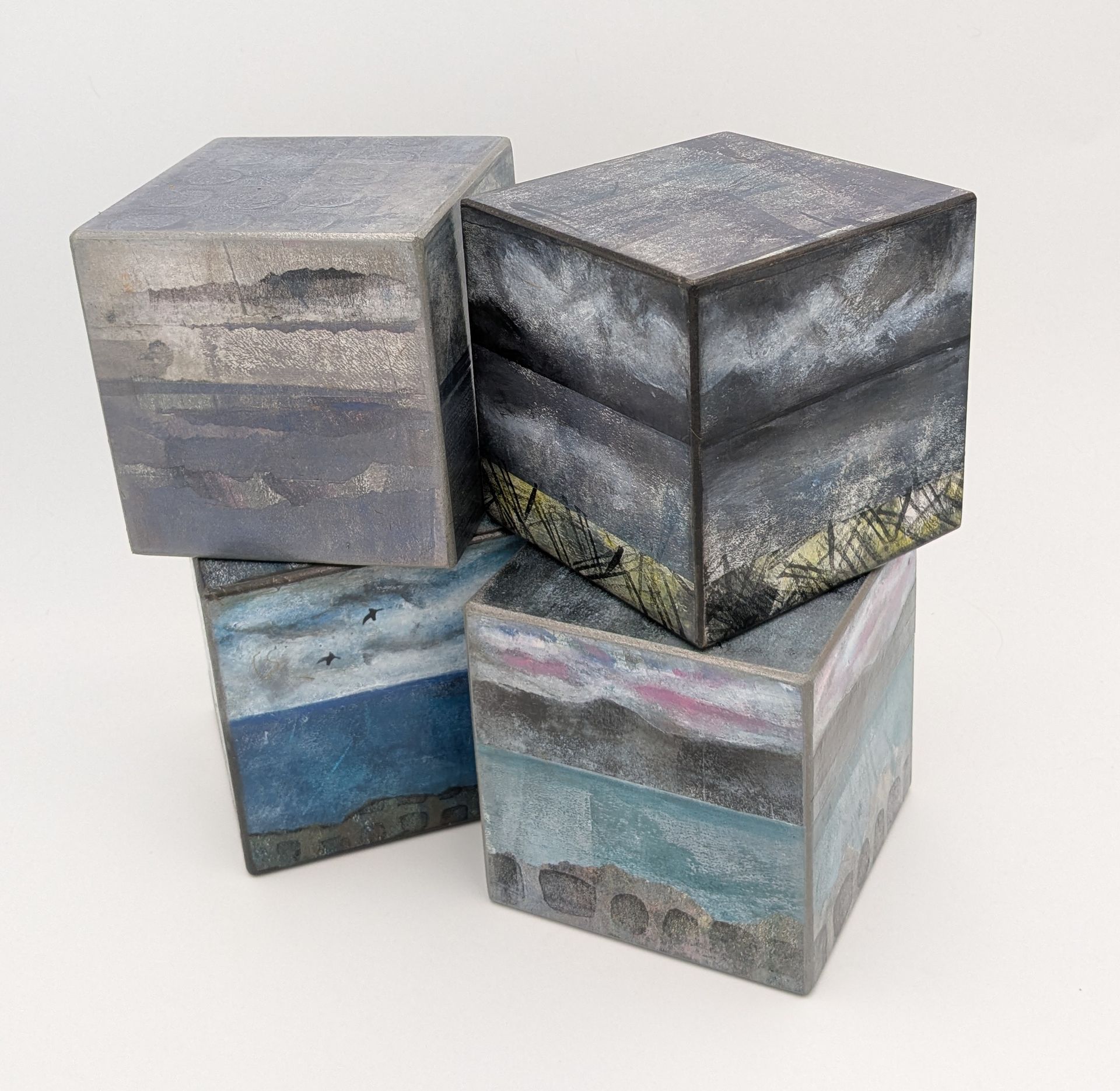 Four square art blocks, stacked and painted with layered landscape scenes in cool tones.