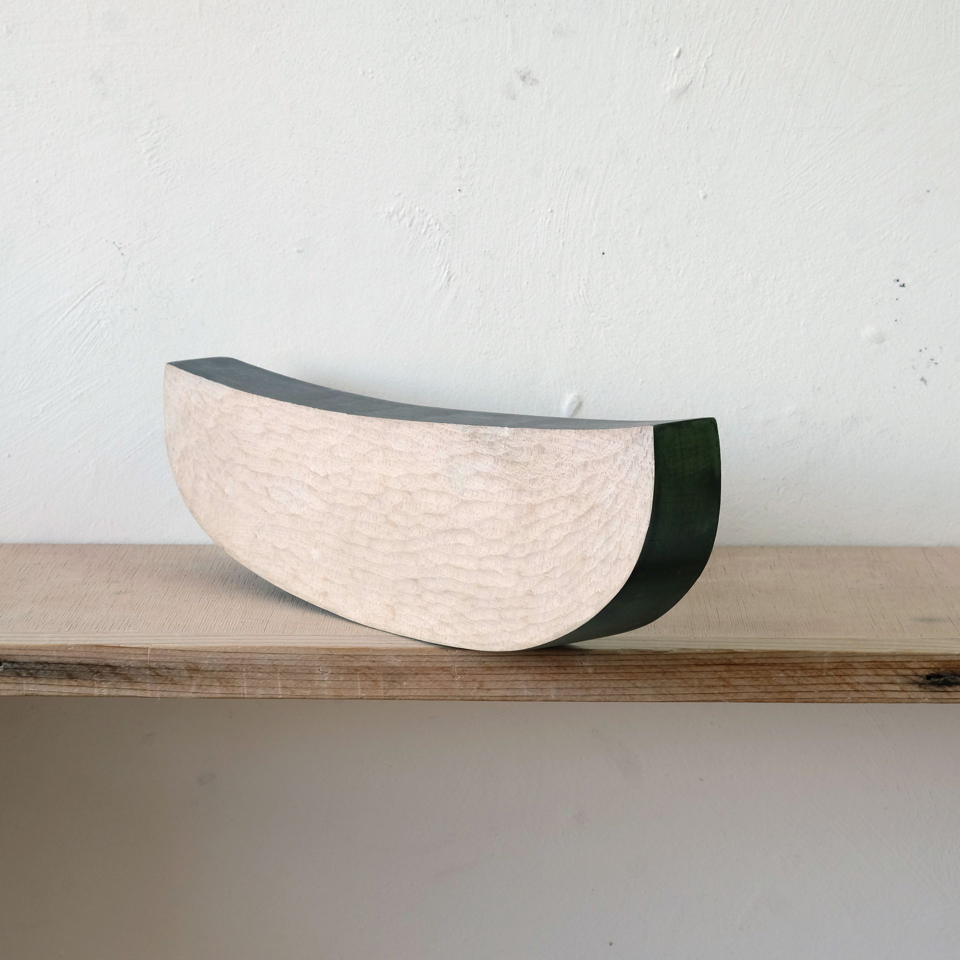 Curved half-cylinder decor piece with cream front and dark green back on a wooden shelf