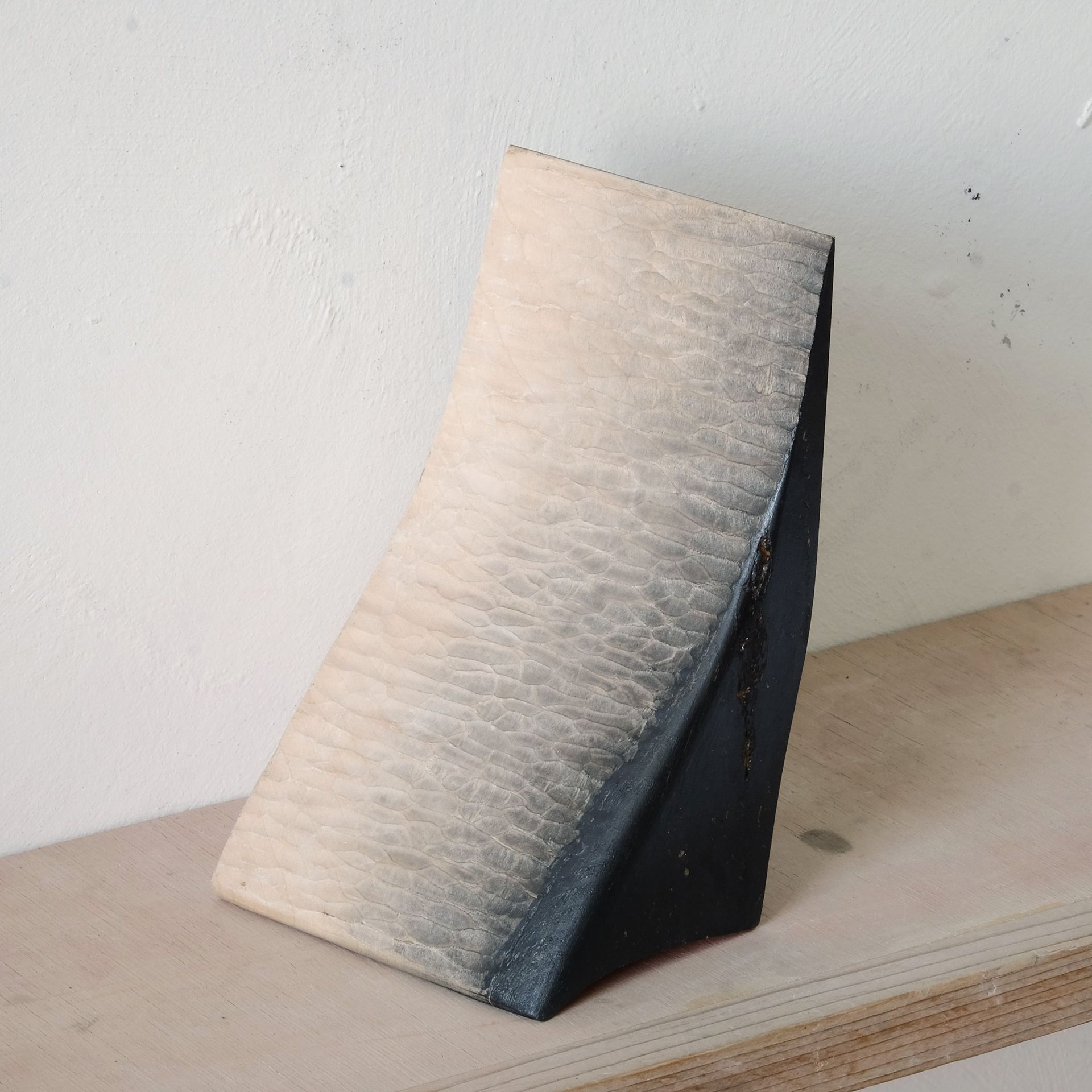A small tilted beige-and-black textured display stand on a tabletop against a white wall.