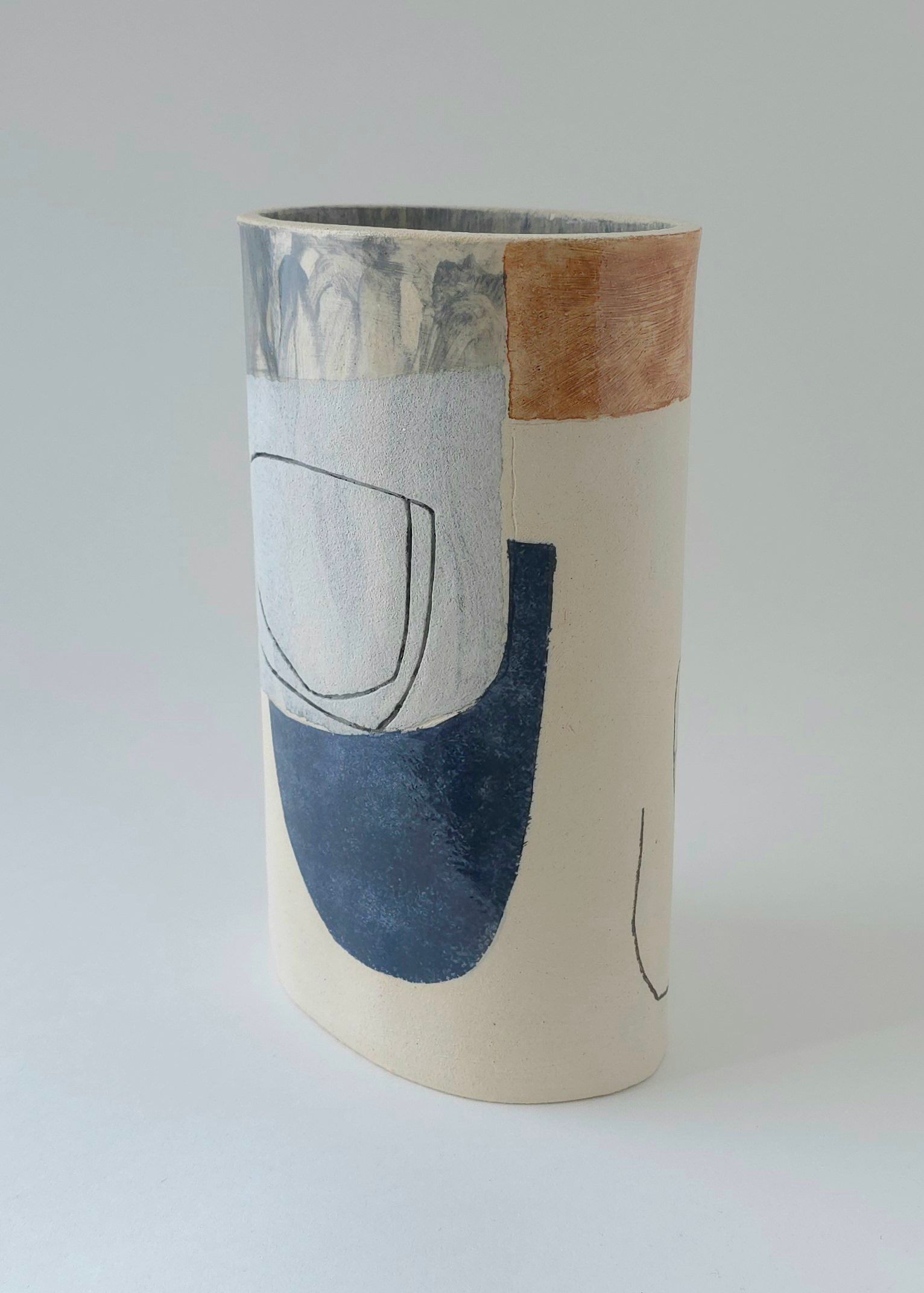 A white vase with a blue and brown design on it is sitting on a white surface.
