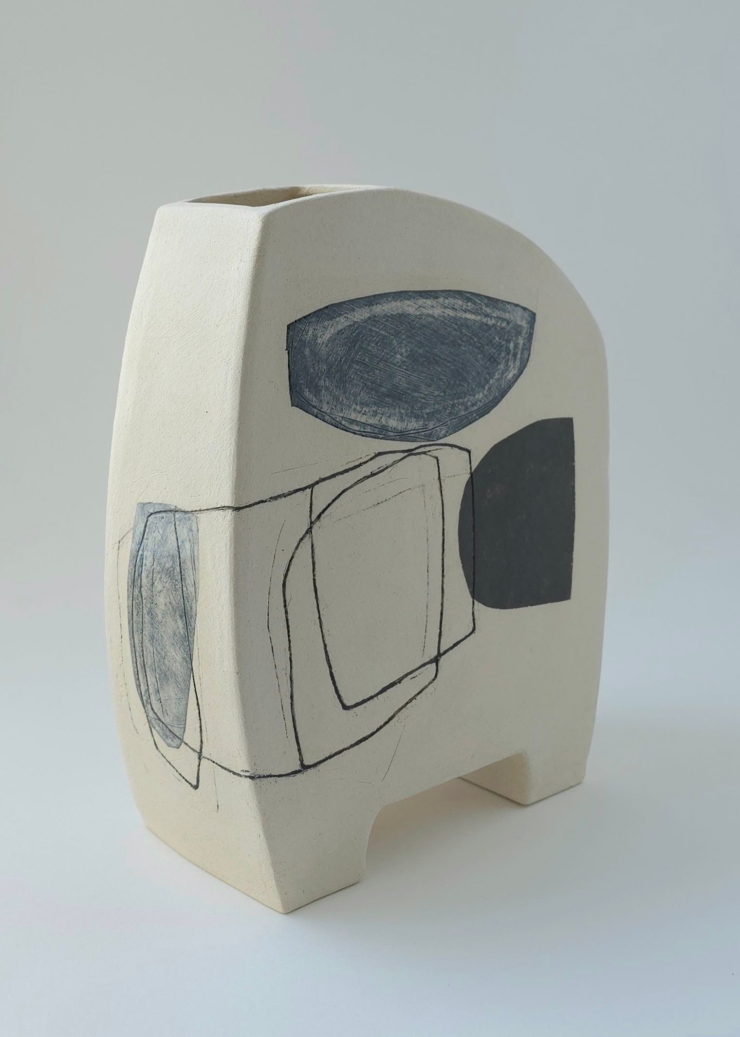 A white vase with a black and white design on it is sitting on a white surface.