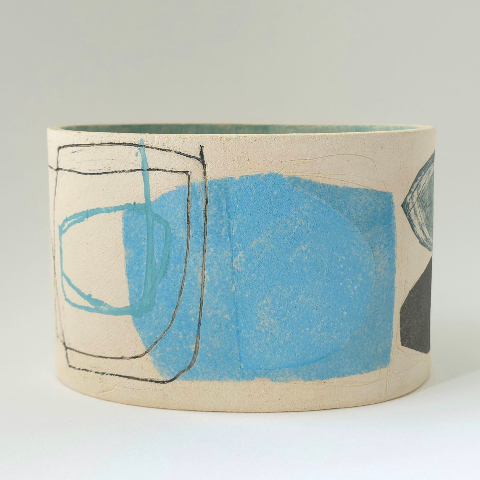 Ceramic cylinder pot with blue, black, and teal abstract shapes and a light green rim.