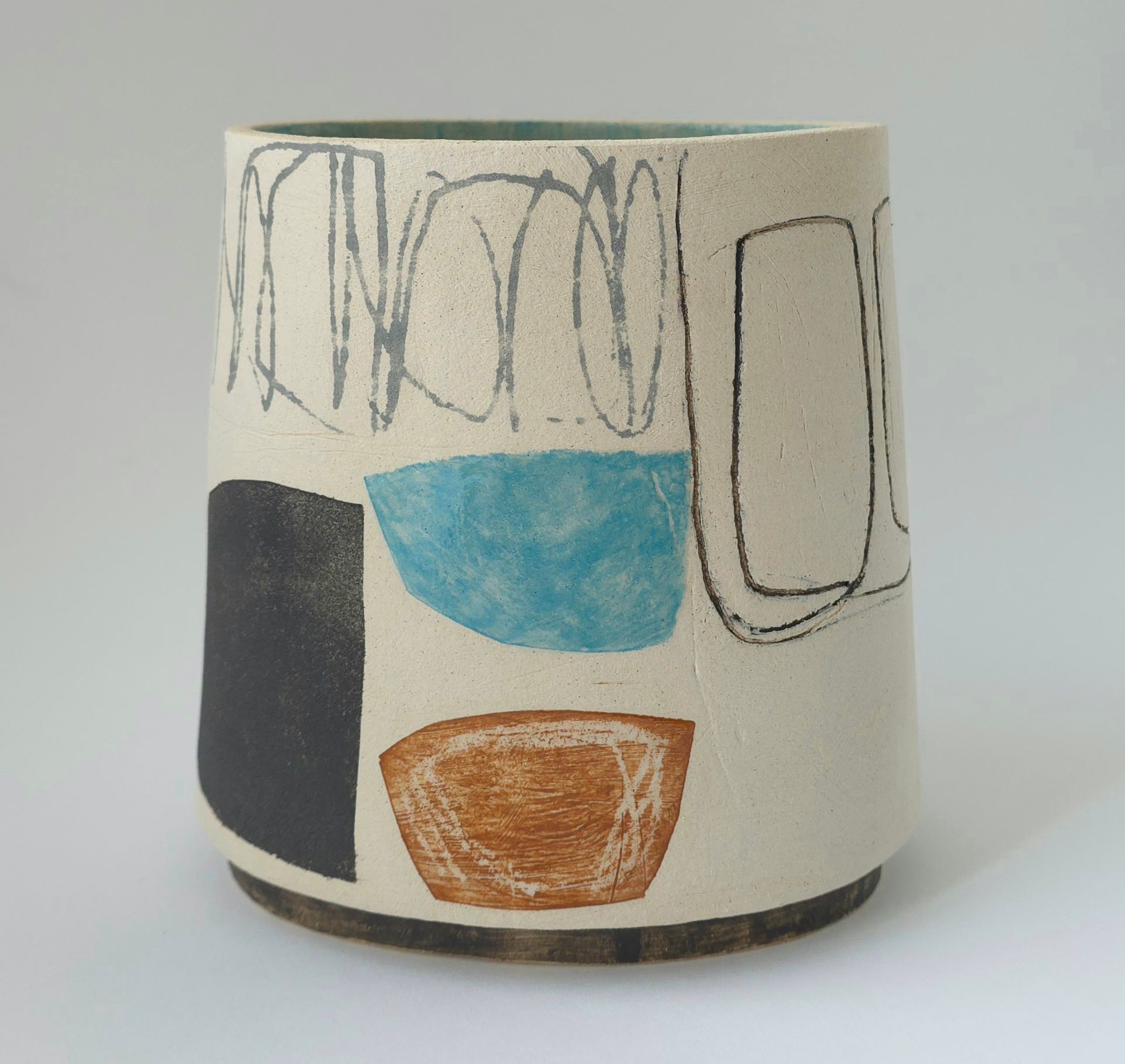 Ceramic cylindrical vase with abstract shapes: black, blue, and orange, with scribbled grey lines on a white background.