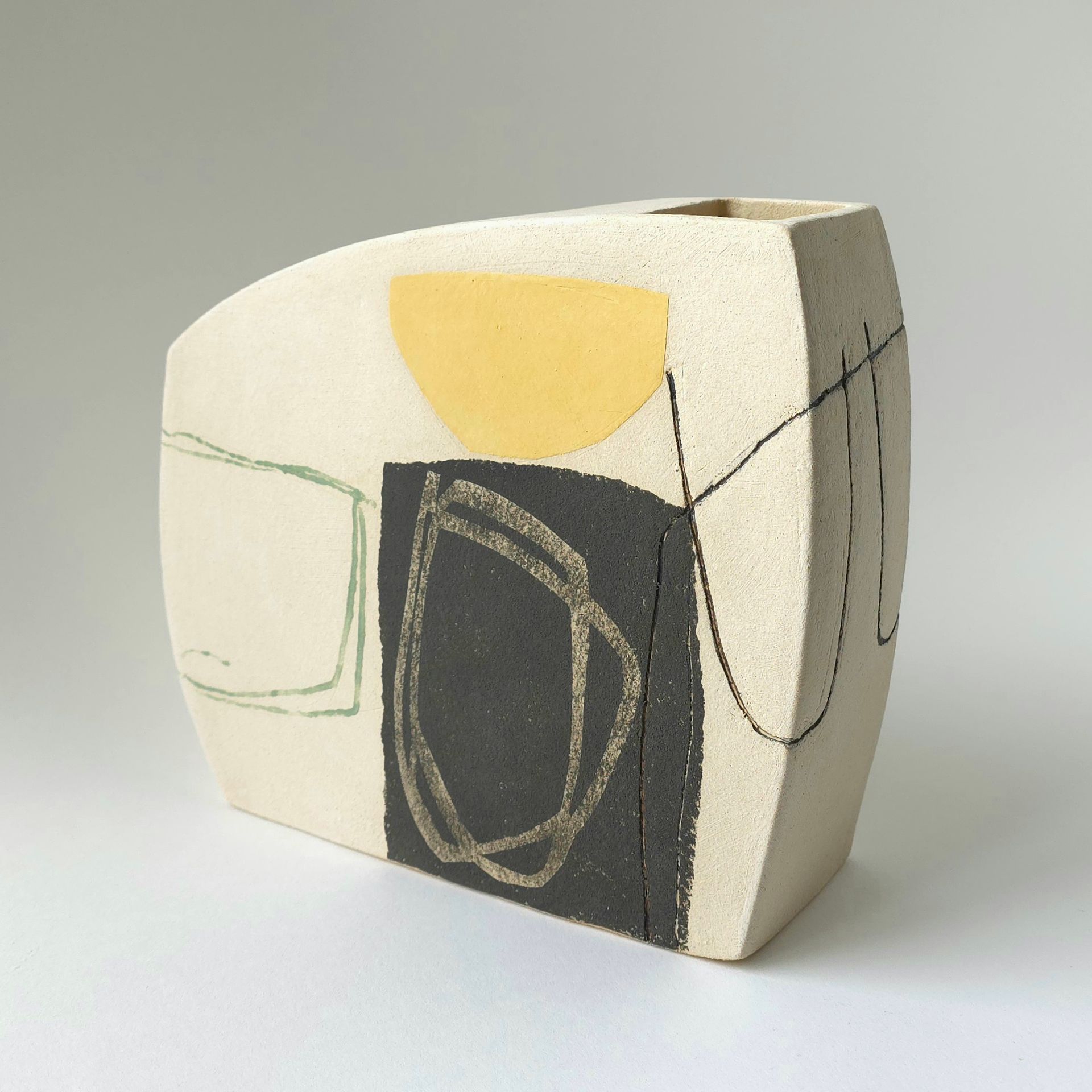 A ceramic vase with a matte cream finish featuring a yellow semi-circle, a black square, and abstract black line art.