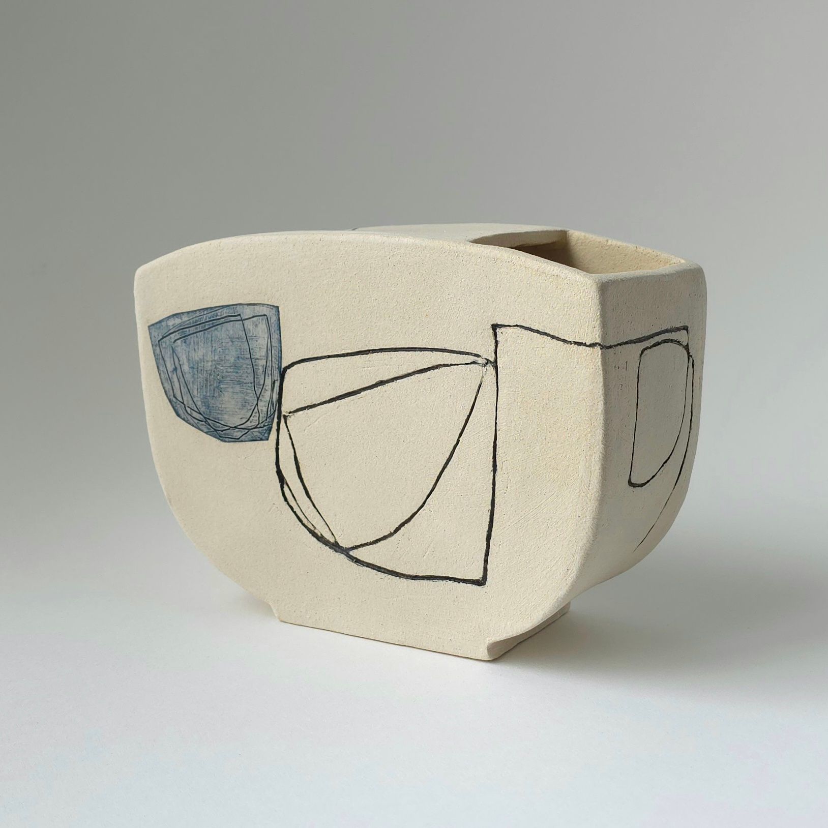 A beige ceramic vase with a textured surface, decorated with hand-drawn black line art and a single muted blue shape.