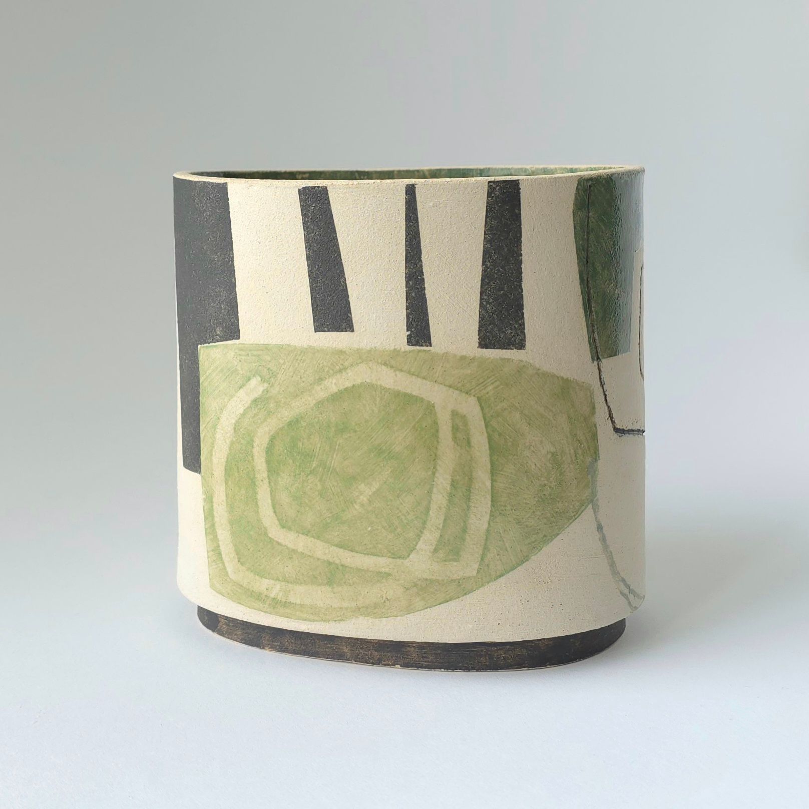 Ceramic vase with abstract black outlines, tan shapes, and blue brushstrokes, set against white.