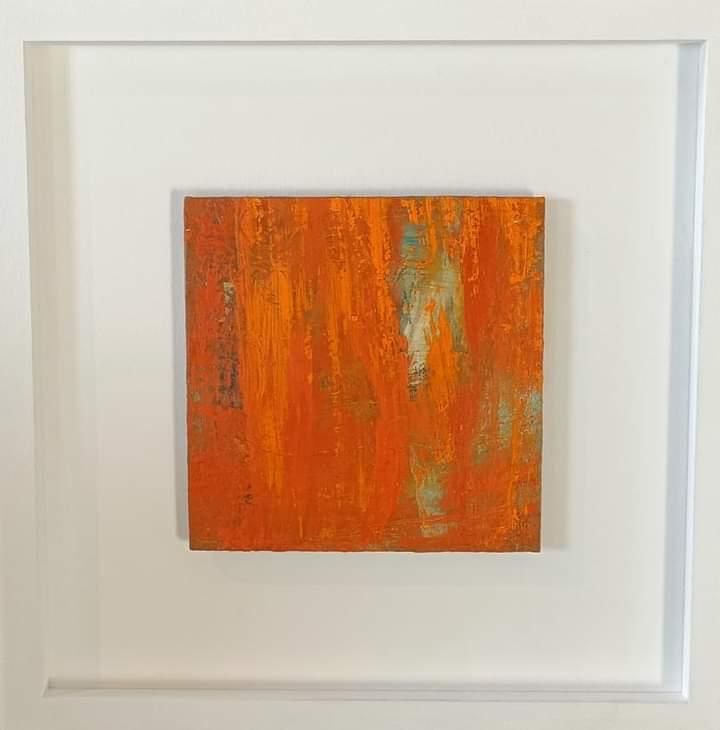 a small orange painting is in a white frame on a wall .