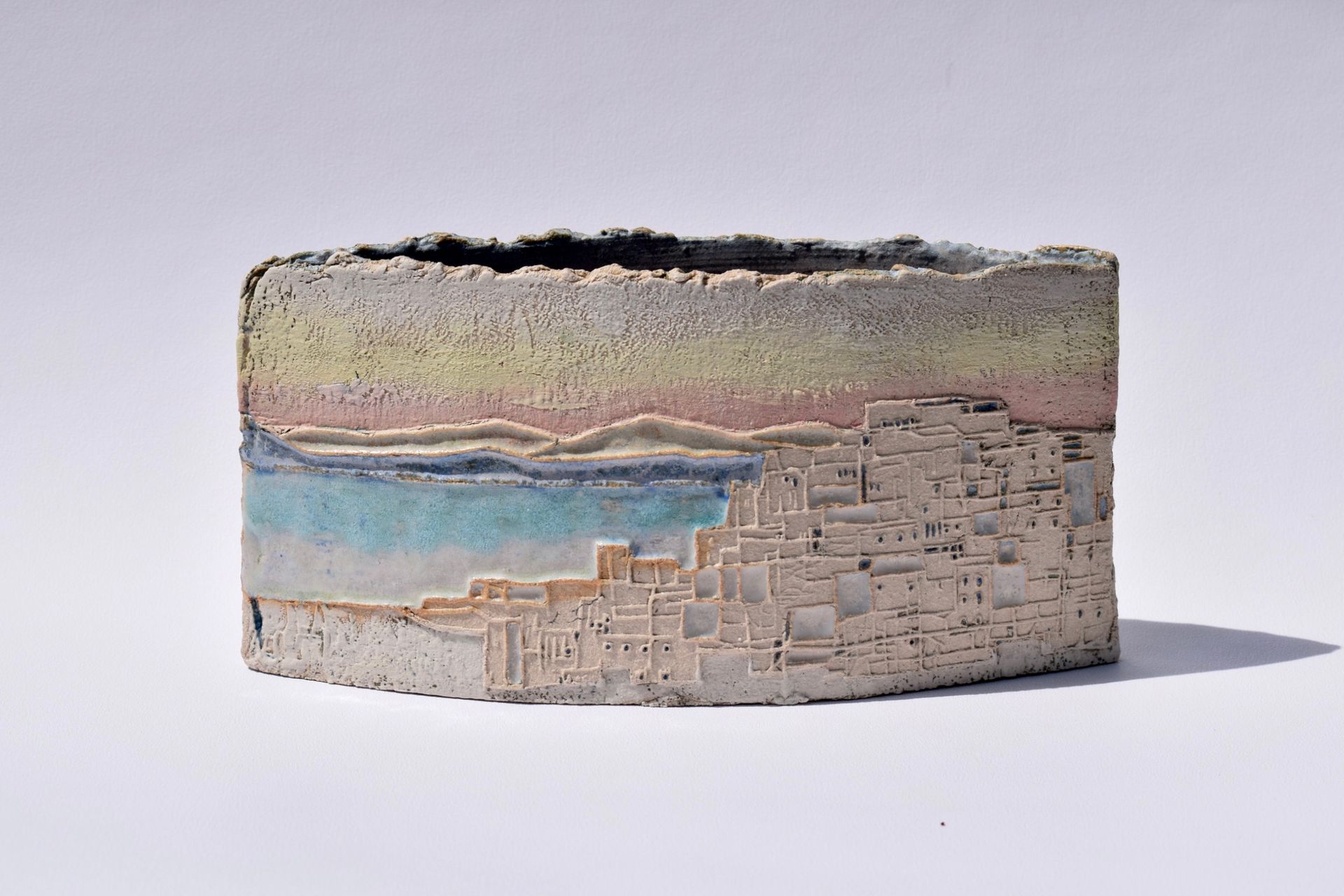 A ceramic sculpture with a landscape on it is sitting on a white surface.