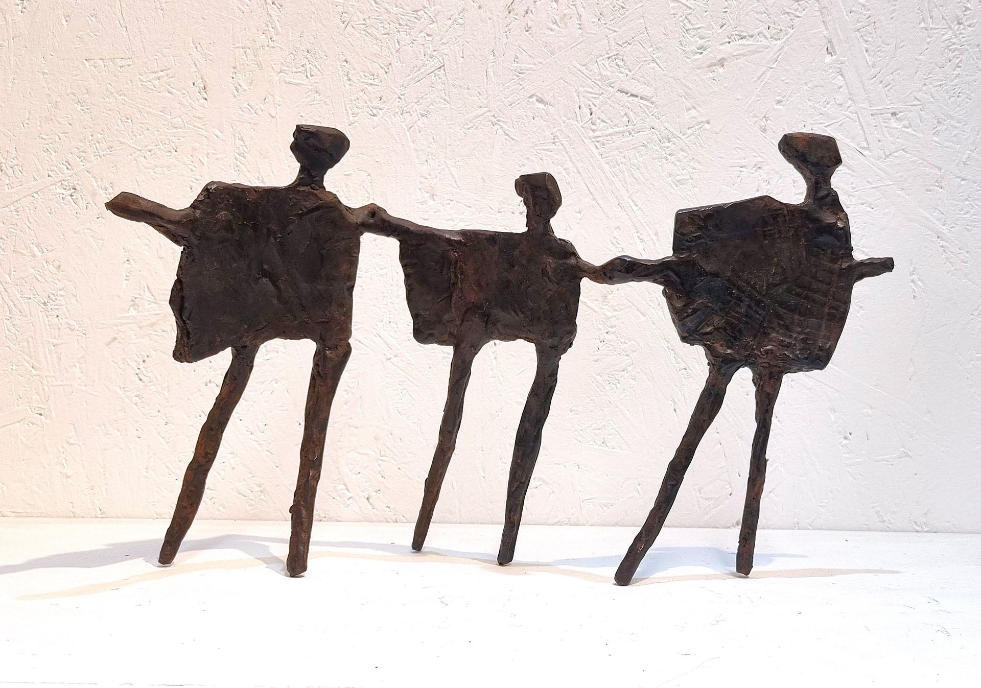 Three abstract black figures linked together against a light wall, like stylized dancers.