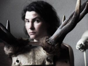 A woman is holding a deer skull in front of her face.