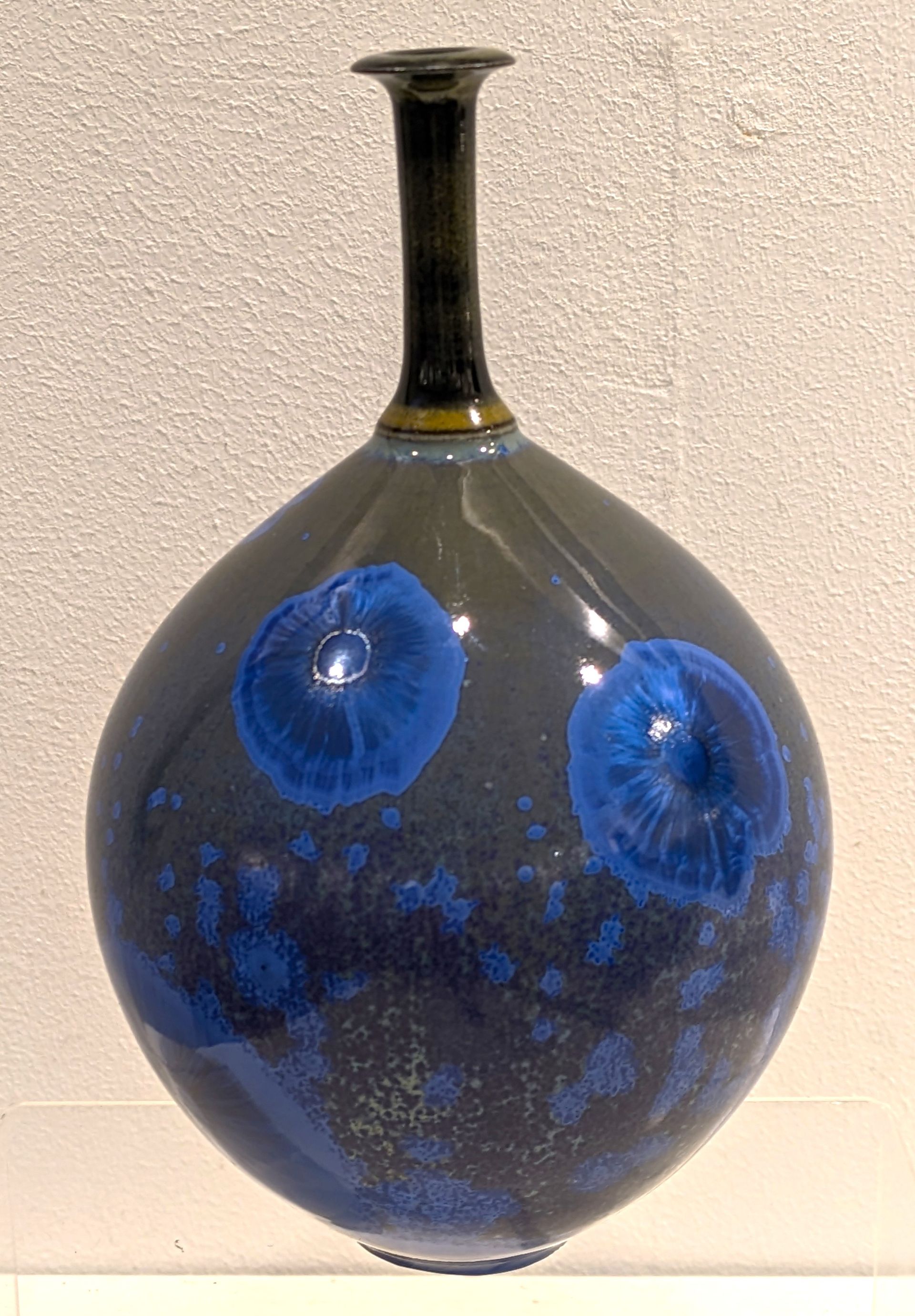 A blue vase with blue circles on it is sitting on a table.