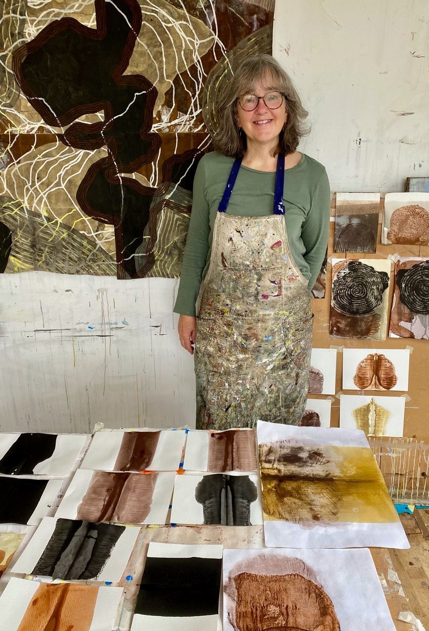 A man with a beard is standing in front of two paintings
