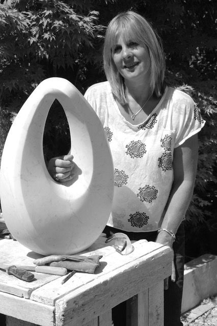 A woman is standing next to a large white egg on a table.