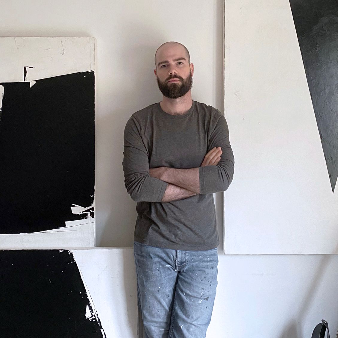 A man with a beard is standing in front of two paintings