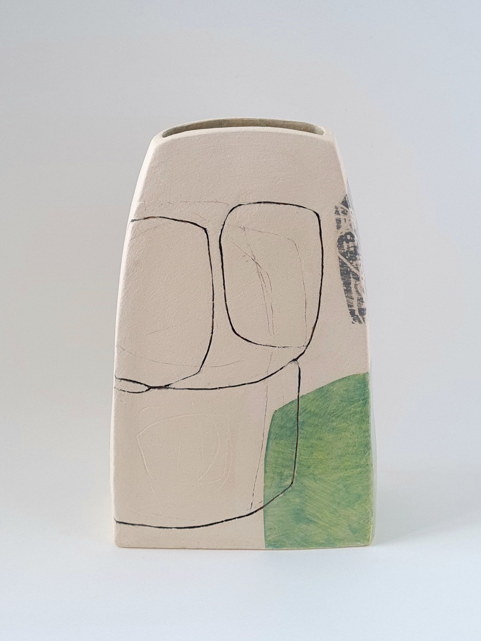 a white vase with a green stripe on the side is sitting on a white surface .