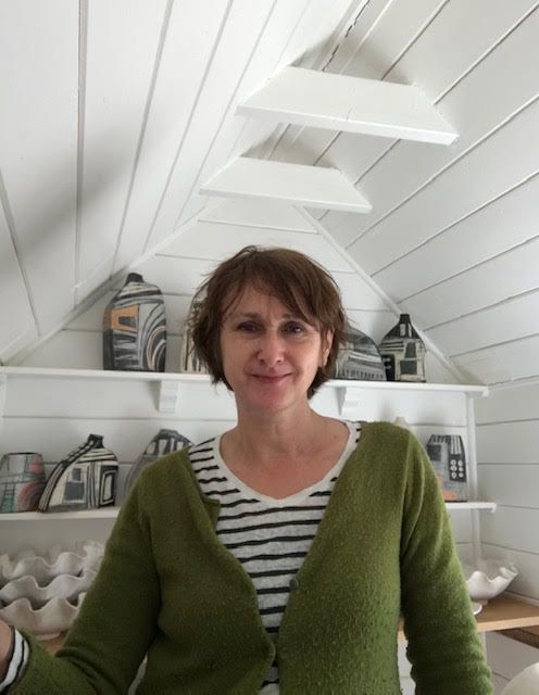 A woman in a green sweater is standing in front of a shelf with houses on it.