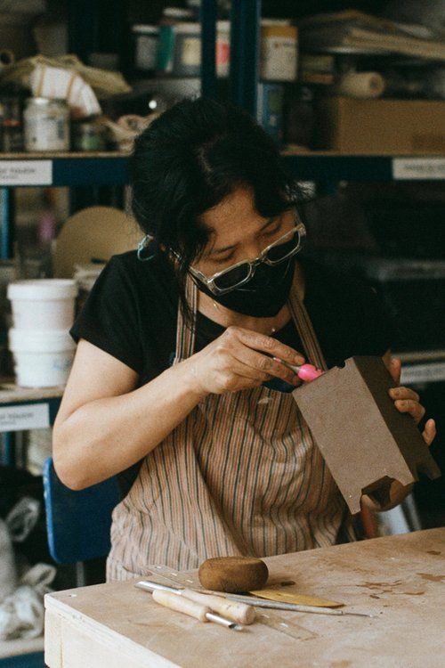 A woman wearing a mask and apron is working on a piece of wood.
