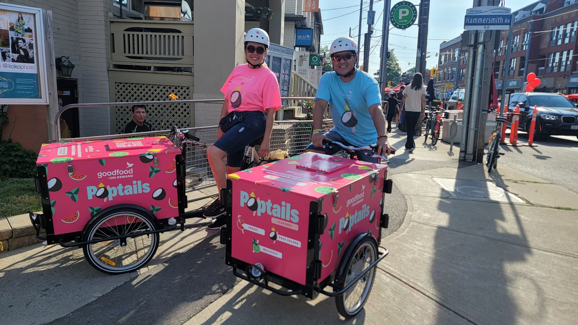 Two people are riding bicycles with pink carts on the side of the road.